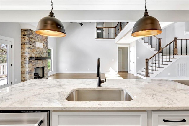 kitchen with sink, dishwasher, hanging light fixtures, light stone counters, and a stone fireplace