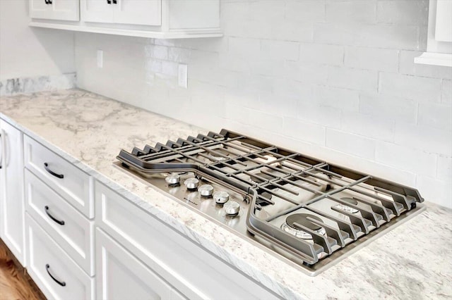 room details featuring stainless steel gas stovetop, white cabinets, and backsplash