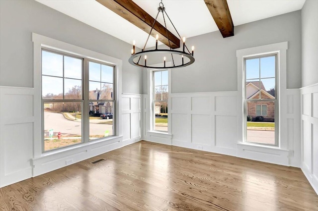 unfurnished dining area with beamed ceiling, wood-type flooring, and a chandelier