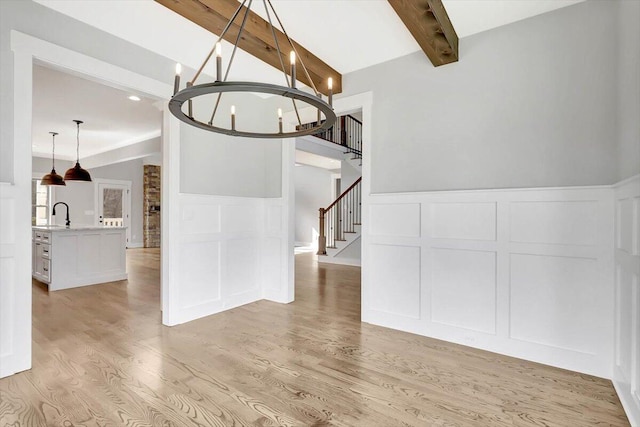 unfurnished dining area with an inviting chandelier, sink, light hardwood / wood-style floors, and vaulted ceiling with beams