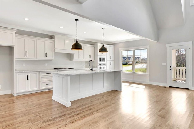 kitchen featuring sink, white cabinetry, an island with sink, decorative light fixtures, and light wood-type flooring