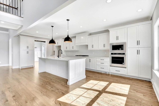 kitchen featuring a kitchen island with sink, built in microwave, oven, and white cabinets