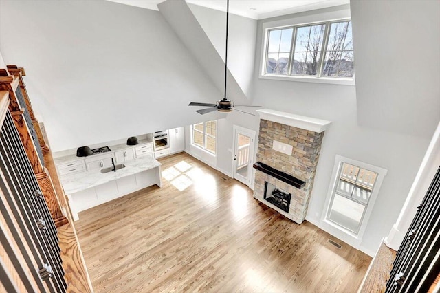 living room with a high ceiling, ceiling fan, a stone fireplace, and light hardwood / wood-style floors