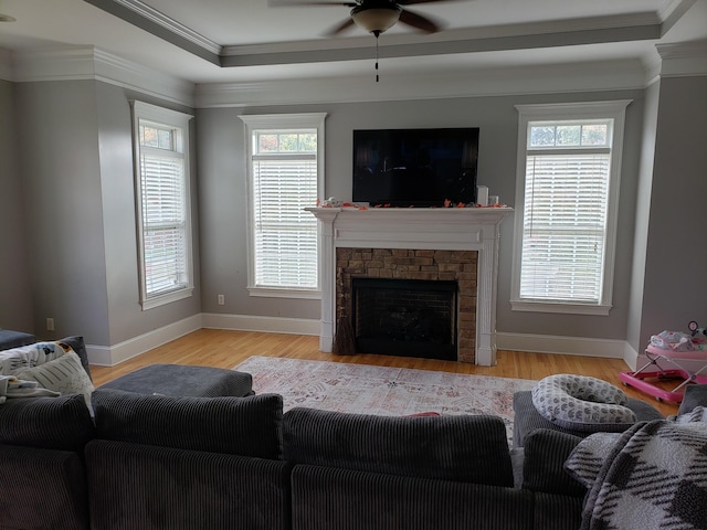 living room featuring ornamental molding, a stone fireplace, light hardwood / wood-style floors, and ceiling fan