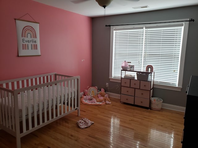 bedroom with a nursery area, hardwood / wood-style flooring, and ceiling fan