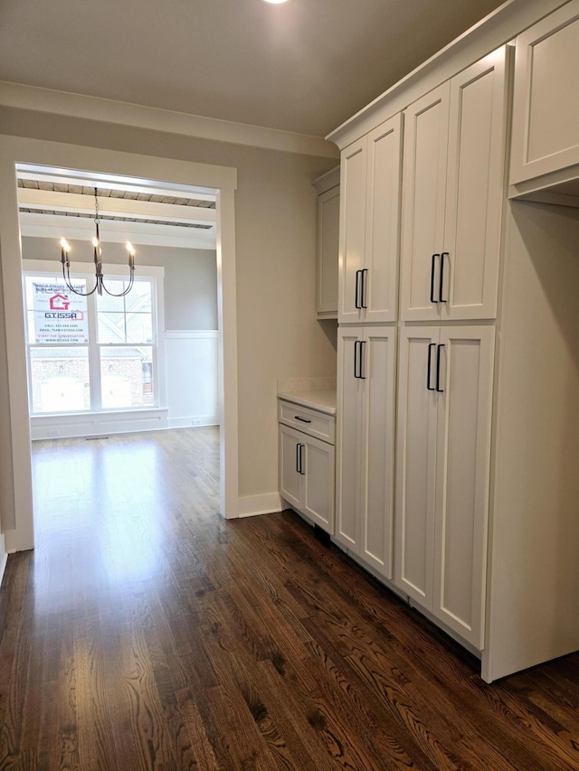 kitchen featuring ornamental molding, decorative light fixtures, a notable chandelier, dark hardwood / wood-style floors, and white cabinetry