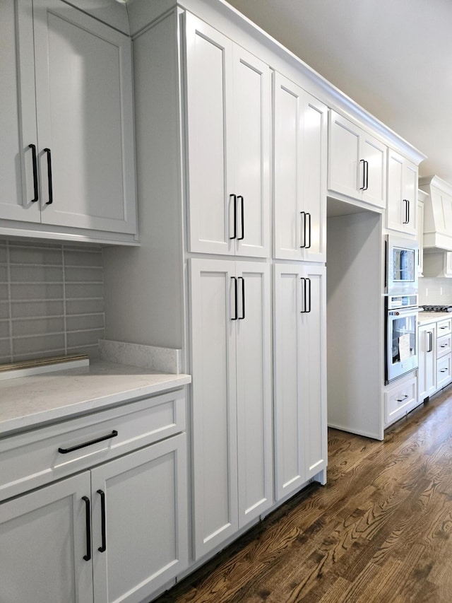 kitchen featuring decorative backsplash, custom range hood, appliances with stainless steel finishes, dark hardwood / wood-style flooring, and white cabinetry