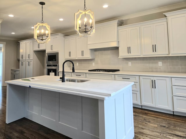 kitchen with a kitchen island with sink, white cabinetry, sink, and pendant lighting