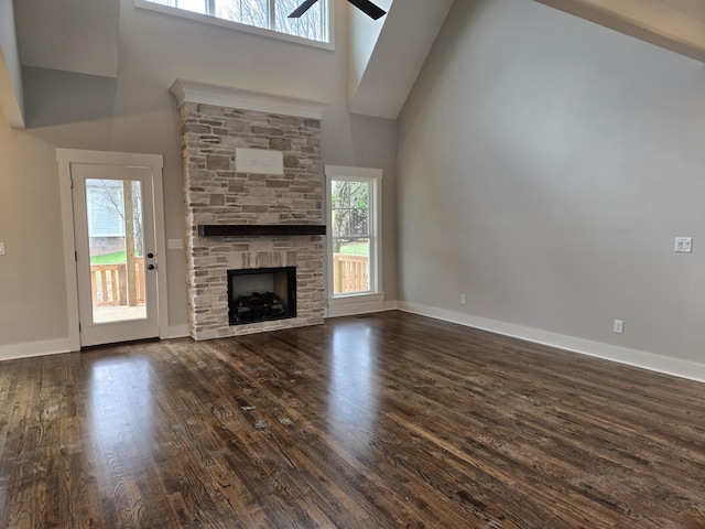 unfurnished living room featuring a towering ceiling, a stone fireplace, ceiling fan, and a healthy amount of sunlight