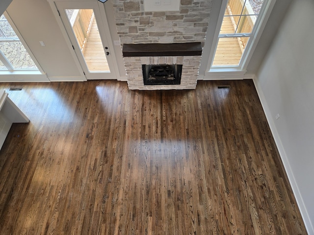 unfurnished living room with a stone fireplace and dark wood-type flooring