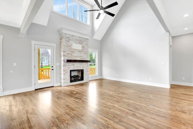 unfurnished living room with a fireplace, light wood finished floors, a high ceiling, ceiling fan, and baseboards