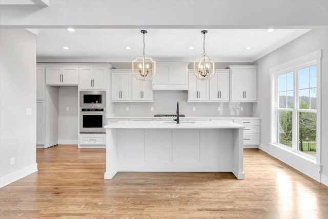 kitchen featuring stainless steel appliances, light countertops, a kitchen island with sink, and white cabinetry