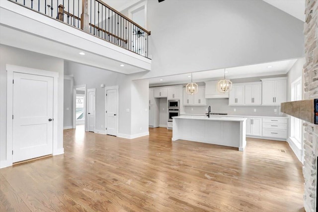 kitchen featuring a kitchen island with sink, white cabinetry, light countertops, appliances with stainless steel finishes, and light wood finished floors