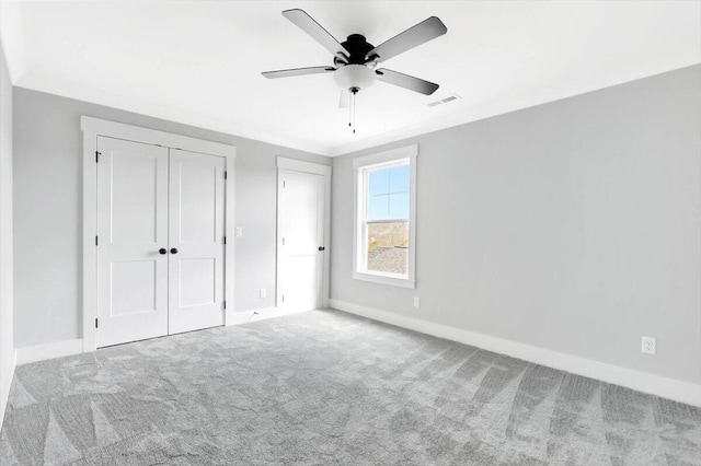 unfurnished bedroom with ceiling fan, light colored carpet, visible vents, baseboards, and ornamental molding