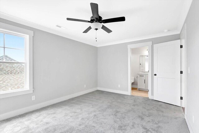 unfurnished bedroom featuring baseboards, visible vents, light colored carpet, ornamental molding, and ensuite bathroom