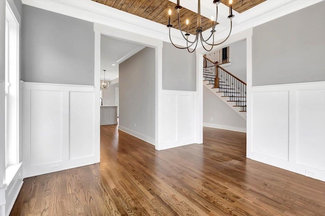 unfurnished dining area with wooden ceiling, stairs, a decorative wall, and wood finished floors