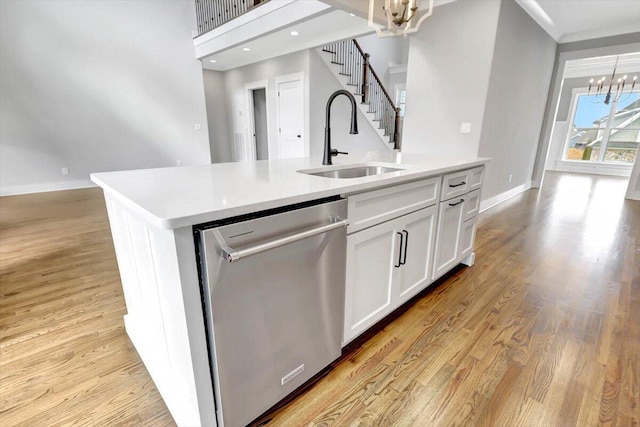 kitchen with dishwasher, a kitchen island with sink, light countertops, white cabinetry, and a notable chandelier