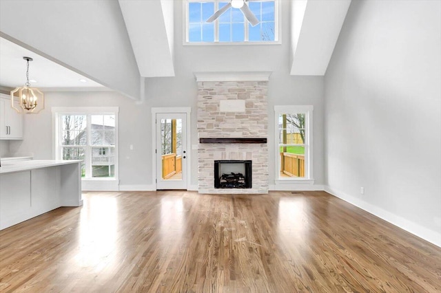 unfurnished living room with ceiling fan with notable chandelier, a fireplace, wood finished floors, and baseboards