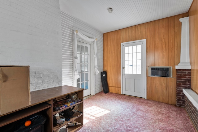 doorway to outside with a wall unit AC, ornate columns, brick wall, carpet, and wood walls