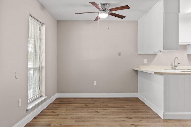 unfurnished dining area with ceiling fan, sink, and light wood-type flooring