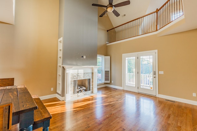 unfurnished living room featuring a tiled fireplace, hardwood / wood-style floors, built in features, high vaulted ceiling, and ceiling fan