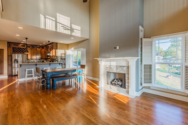 dining area with a tile fireplace, hardwood / wood-style floors, a towering ceiling, and plenty of natural light