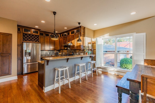 kitchen featuring kitchen peninsula, stainless steel refrigerator with ice dispenser, decorative light fixtures, dark hardwood / wood-style flooring, and tasteful backsplash