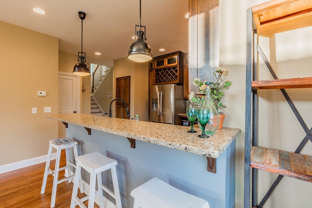 kitchen with stainless steel refrigerator with ice dispenser, wood-type flooring, a breakfast bar, decorative light fixtures, and light stone counters