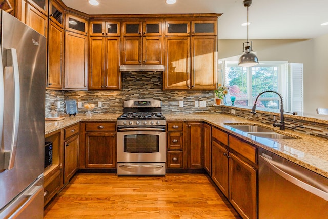 kitchen with sink, stainless steel appliances, decorative light fixtures, light stone counters, and light hardwood / wood-style flooring