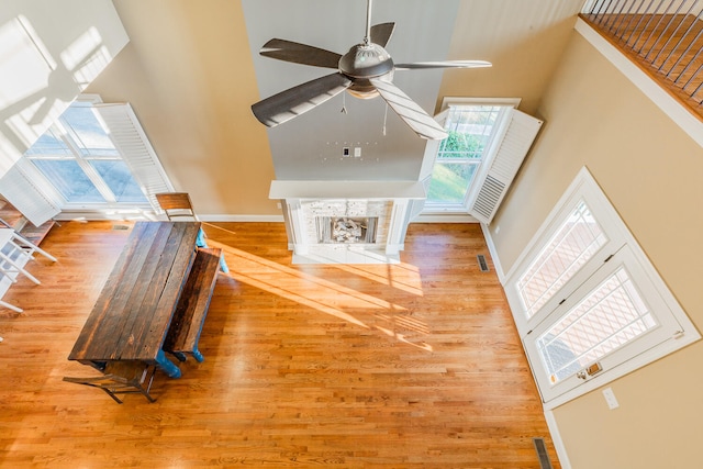 living room with a towering ceiling, hardwood / wood-style flooring, a tile fireplace, and ceiling fan