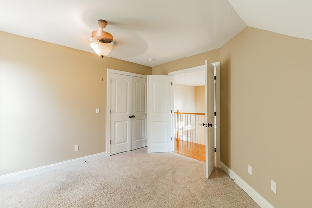 unfurnished bedroom with a closet, light colored carpet, vaulted ceiling, and ceiling fan