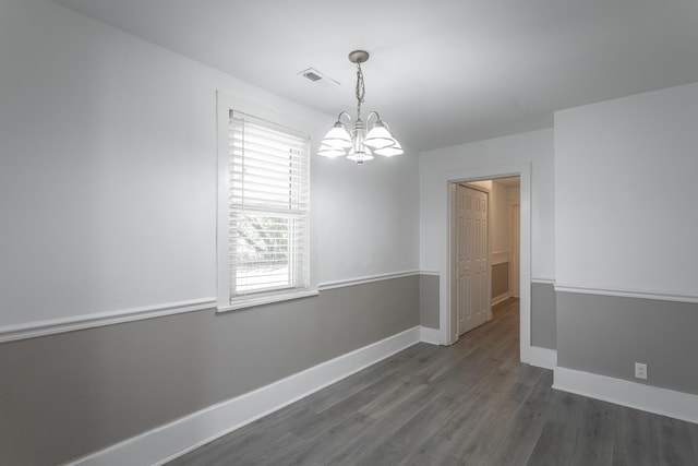 spare room featuring a chandelier and dark wood-type flooring