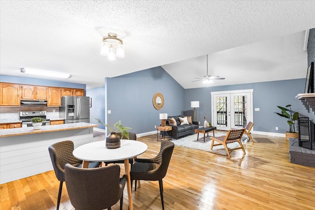 dining room featuring a brick fireplace, a textured ceiling, light hardwood / wood-style flooring, and lofted ceiling