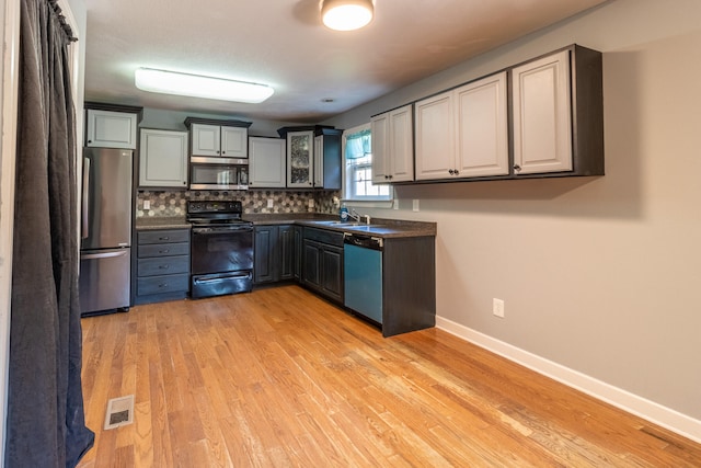 kitchen featuring appliances with stainless steel finishes, light wood-type flooring, tasteful backsplash, sink, and gray cabinets