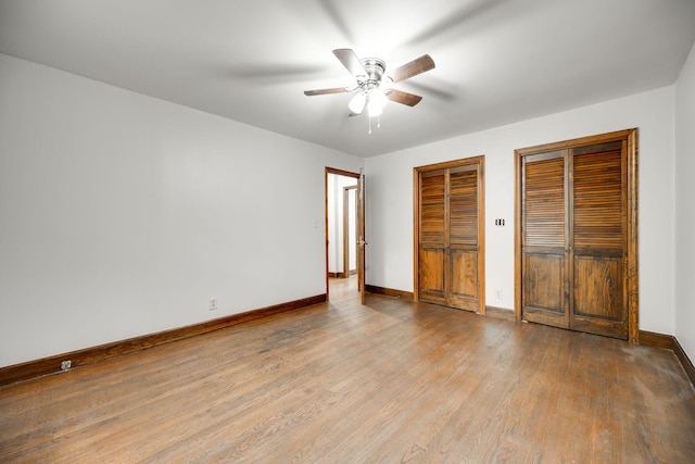 unfurnished bedroom with hardwood / wood-style flooring, ceiling fan, and multiple closets