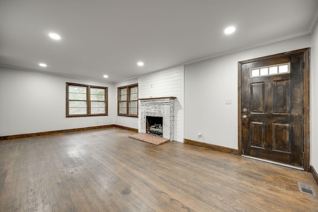 unfurnished living room featuring dark wood-type flooring, ornamental molding, and a brick fireplace