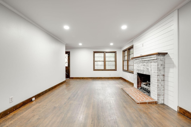 unfurnished living room featuring hardwood / wood-style floors, ornamental molding, and a brick fireplace