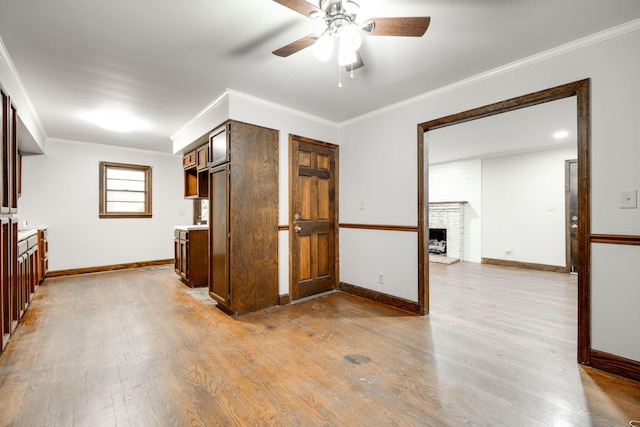 interior space with a brick fireplace, ceiling fan, crown molding, dark brown cabinets, and light wood-type flooring