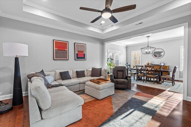 living room featuring ornamental molding, wood-type flooring, ceiling fan with notable chandelier, and a raised ceiling