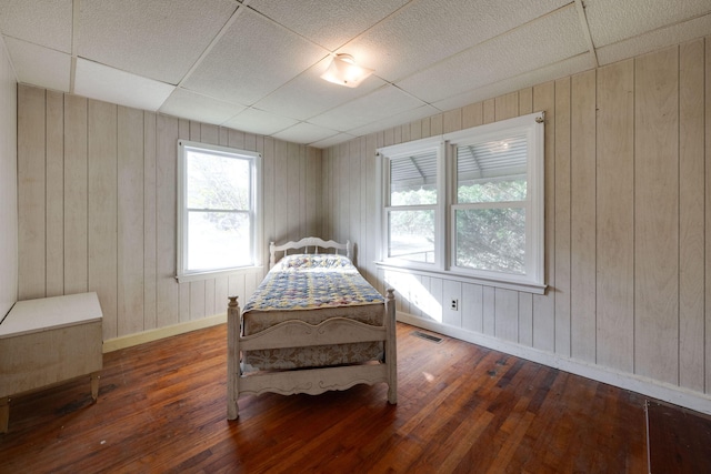 bedroom featuring a drop ceiling, wooden walls, and dark hardwood / wood-style floors