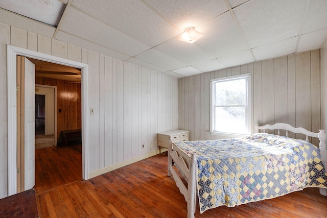 bedroom featuring a paneled ceiling, wood walls, and dark hardwood / wood-style floors