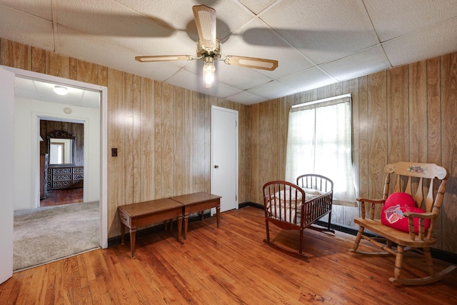 sitting room with ceiling fan, wood walls, and wood-type flooring