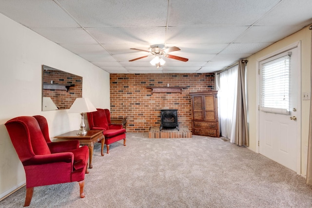 sitting room with a drop ceiling, carpet floors, a wood stove, and ceiling fan