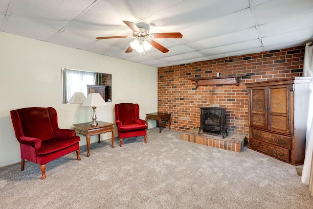 living area with a drop ceiling, a wood stove, carpet, and ceiling fan