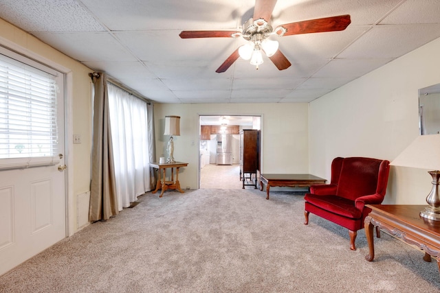 living area featuring a paneled ceiling, carpet, and ceiling fan