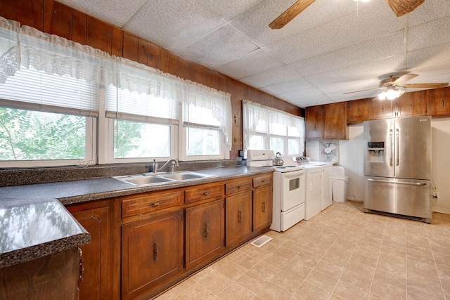 kitchen with ceiling fan, a paneled ceiling, stainless steel refrigerator with ice dispenser, sink, and washer and clothes dryer