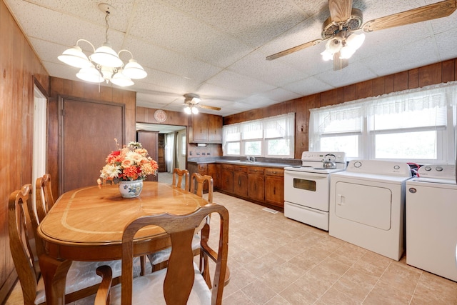 dining room with wood walls, washing machine and dryer, sink, a drop ceiling, and ceiling fan with notable chandelier