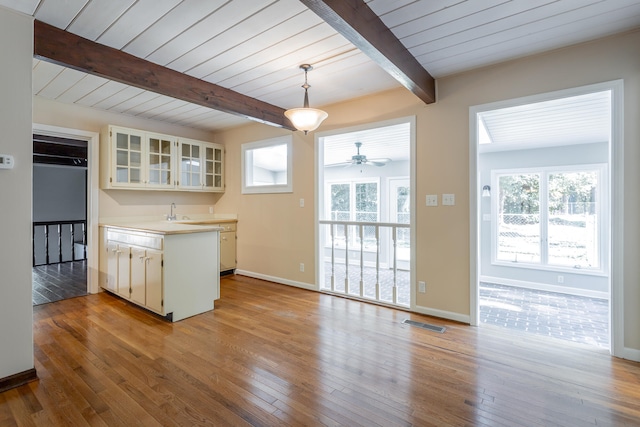 kitchen with hanging light fixtures, white cabinetry, light wood-type flooring, beamed ceiling, and sink