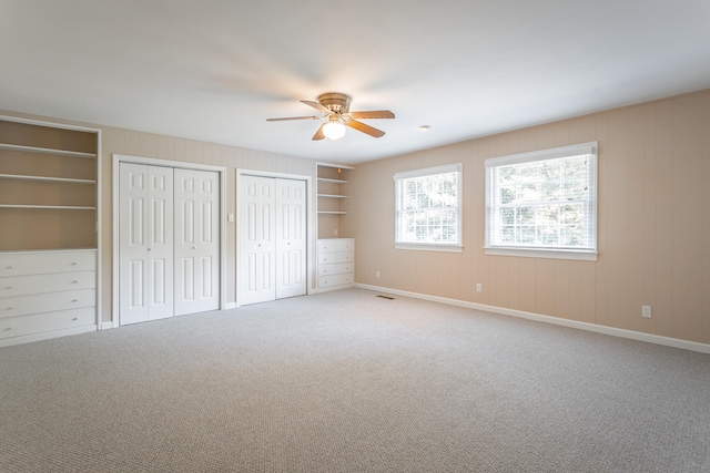 unfurnished bedroom featuring ceiling fan, multiple closets, and carpet floors