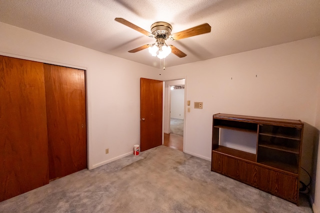 unfurnished bedroom featuring light carpet, a closet, a textured ceiling, and ceiling fan